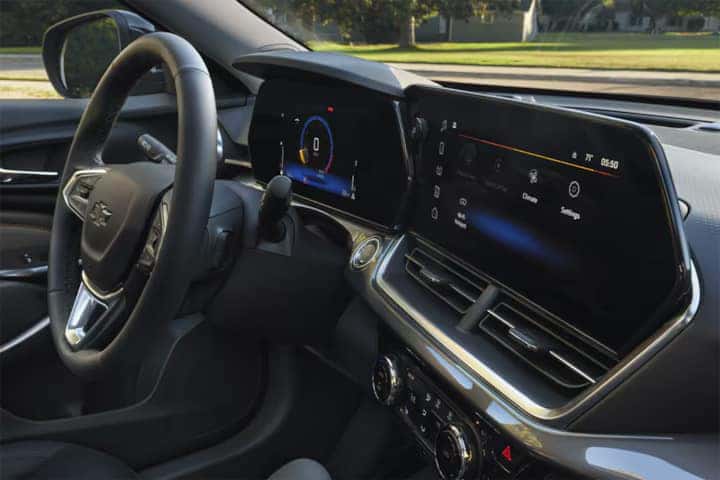 Interior view of a modern car showing the dashboard and steering wheel. The digital display and infotainment screen are active, with visible controls. Black leather seats and paneling create a sleek, sophisticated look. The outside view shows a park setting.