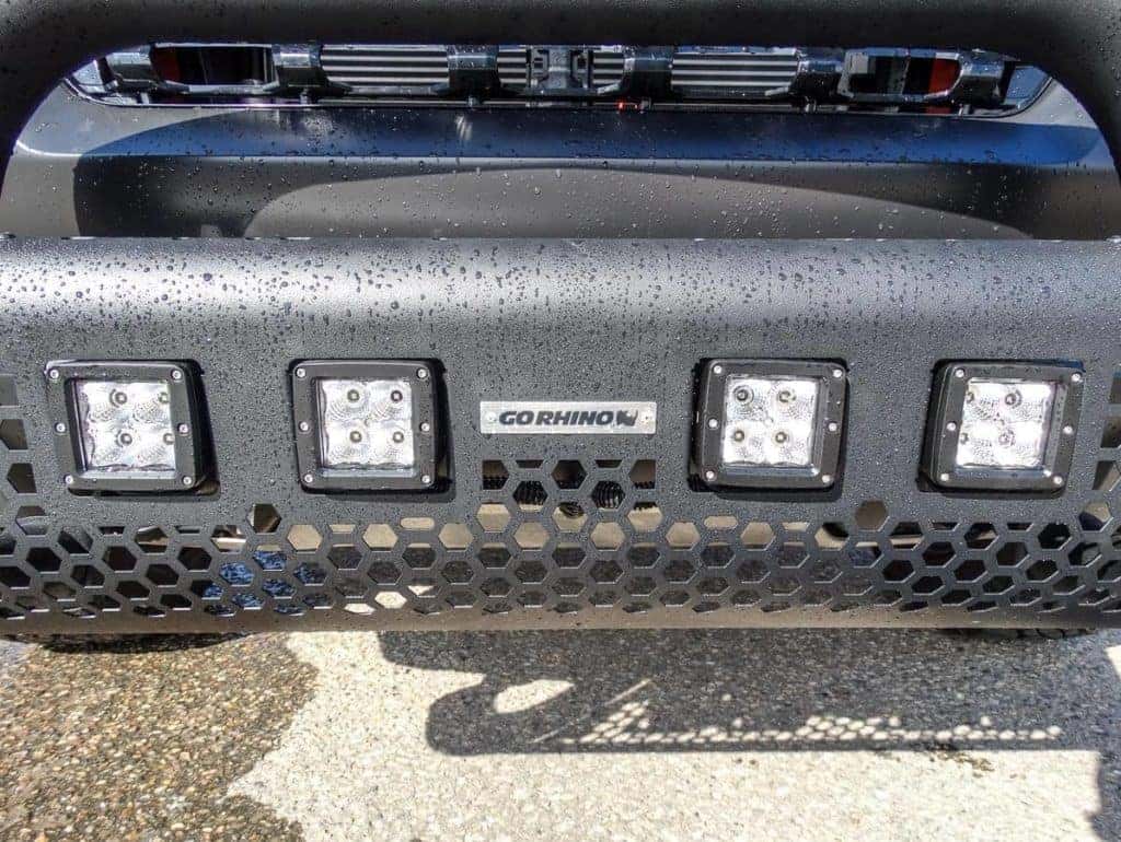 Close-up of a wet metal vehicle grille with four LED lights and "Go Rhino" branding.