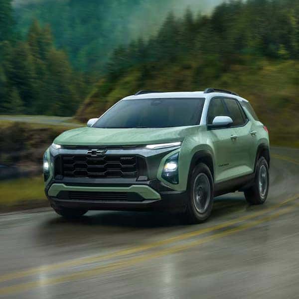 A dark SUV is parked on a rugged desert landscape with rocky formations and distant mountains under a cloudy sky. The car is viewed from the side, highlighting its sleek design and shiny wheels.
