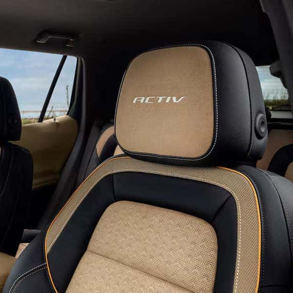 Luxury vehicle interior with three rows of brown leather seats. The seats have Ultimate labels, prominent stitching, and headrests. The background shows a blurred outdoor landscape through large windows.