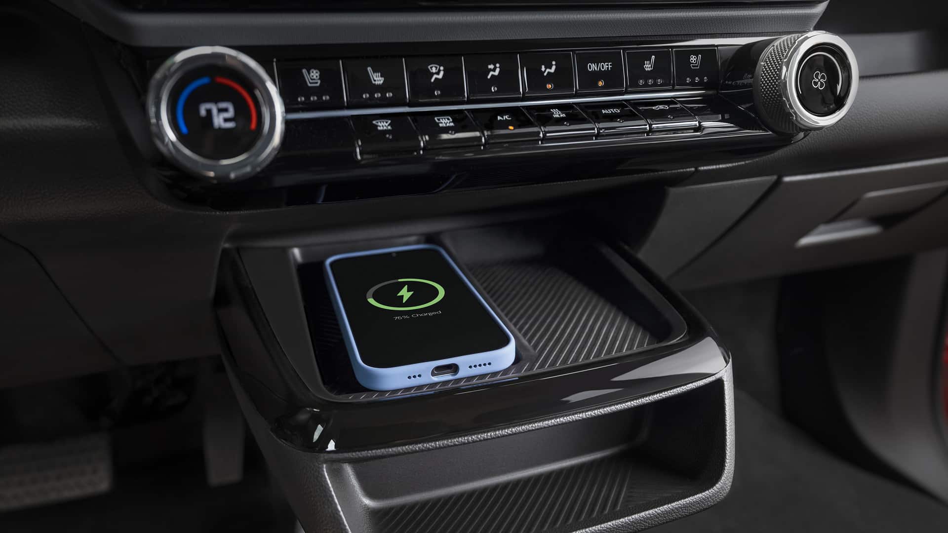 Smartphone charging wirelessly in car tray, surrounded by climate control buttons and temperature dial.