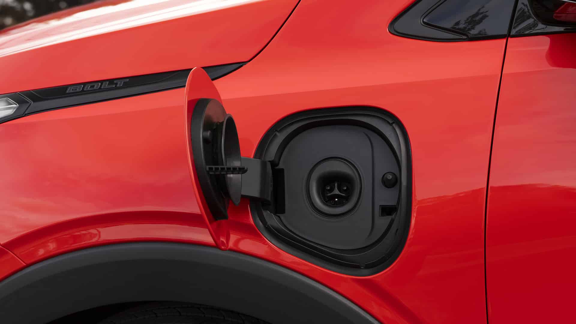 Red electric car's open charging port, highlighting the Bolt model name on the side.