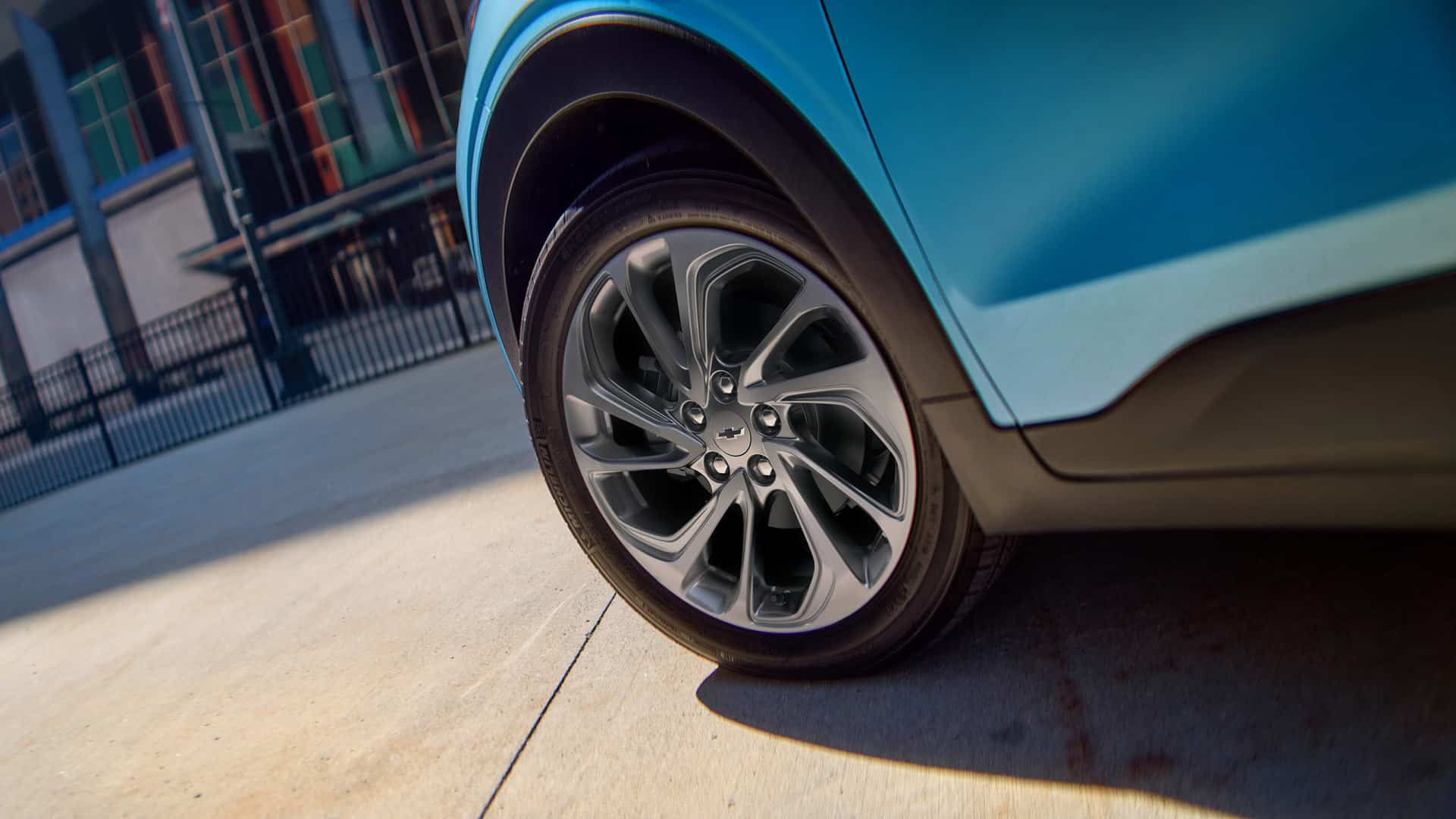 Close-up of a blue car's alloy wheel on a sunny day, parked near a building.