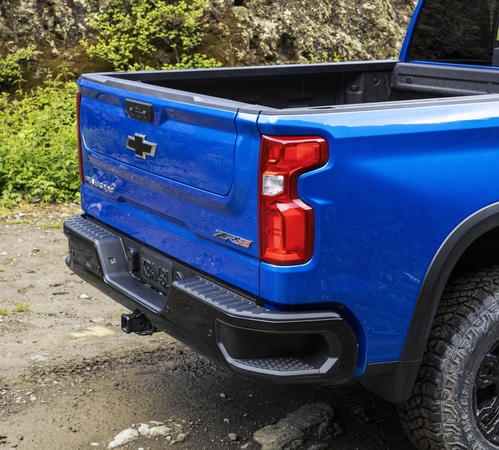 Blue pickup truck parked on a dirt path, showcasing its open cargo bed and rear design.