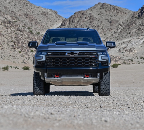 A black pickup truck on a rocky desert landscape with mountains in the background.