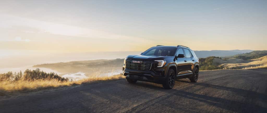 Black SUV driving on a scenic road during sunset, with rolling hills and a coastal view.