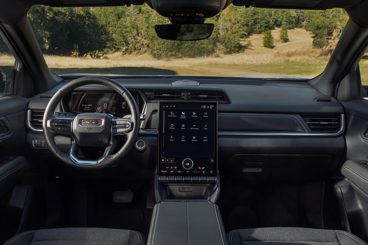 The image shows the interior of a modern car, featuring a steering wheel, a digital dashboard, and a large touchscreen display on the center console. The display shows various controls and settings. The car has a sleek, black design.