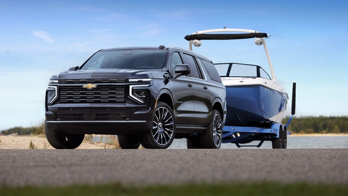 SUV towing a blue boat on a trailer by a lakeside, highlighting its towing capacity.