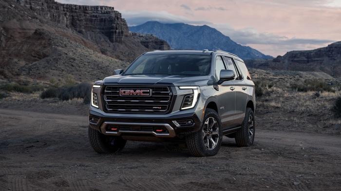 GMC SUV parked on a rugged, mountainous landscape during sunset.