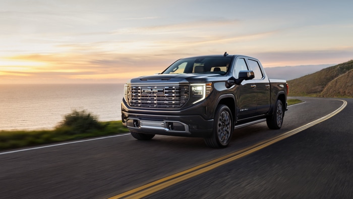 Black pickup truck driving on a coastal road at sunset, showcasing its sleek design and powerful build.