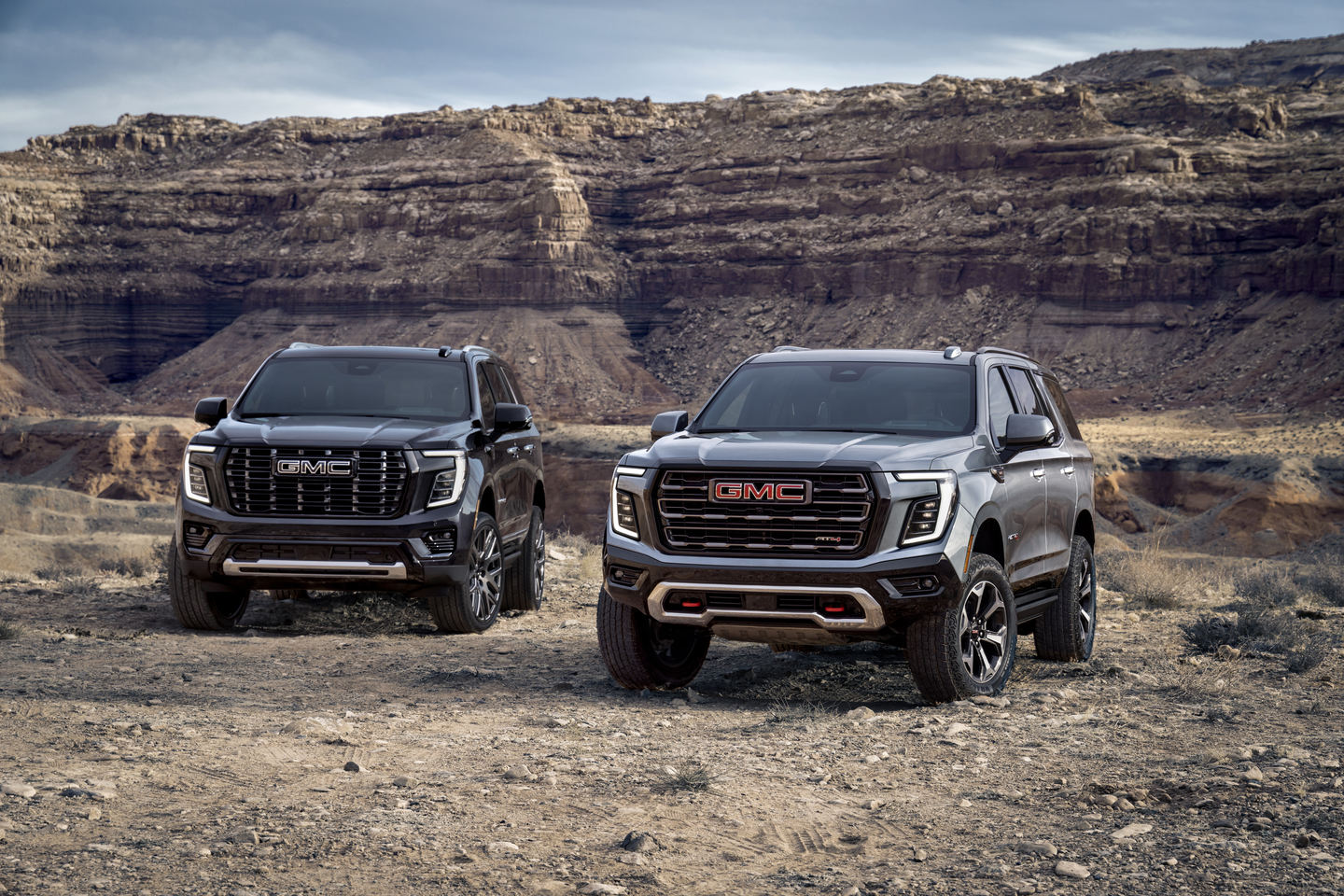 Two GMC SUVs parked against a rugged canyon backdrop under a clear sky.