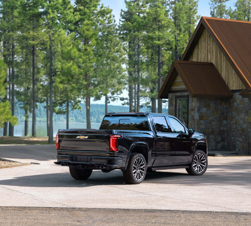 Black pickup truck parked near a wooden cabin with a forest backdrop.