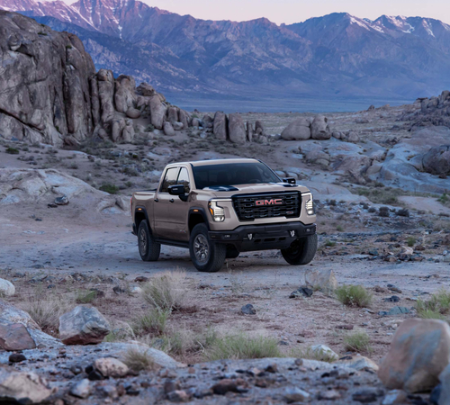 A GMC truck navigating rocky terrain with mountains in the background, showcasing its off-road capability.