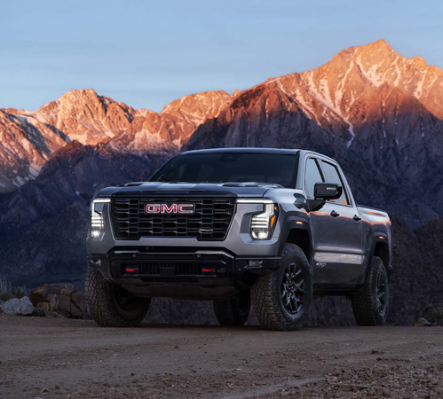 A gray GMC pickup truck on a rugged dirt path with majestic mountains in the background at sunset.